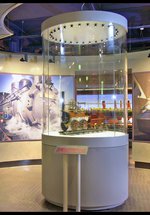 Circular glass case displaying an early steam engine model, with large photo's of different locomotive engines displayed on the wall