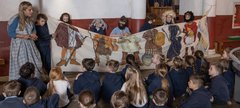 Class of children, some sitting on the floor, others standing behind a large strip of cloth