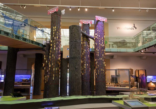 Installation artwork in a museum. Gold metal tags hung from red cords attached to columns