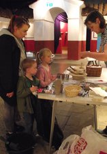 A woman demonstrates a craft activity to two children and an adult at a table in the Roman Gallery