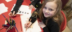Girl sitting at a red table colouring in some paper