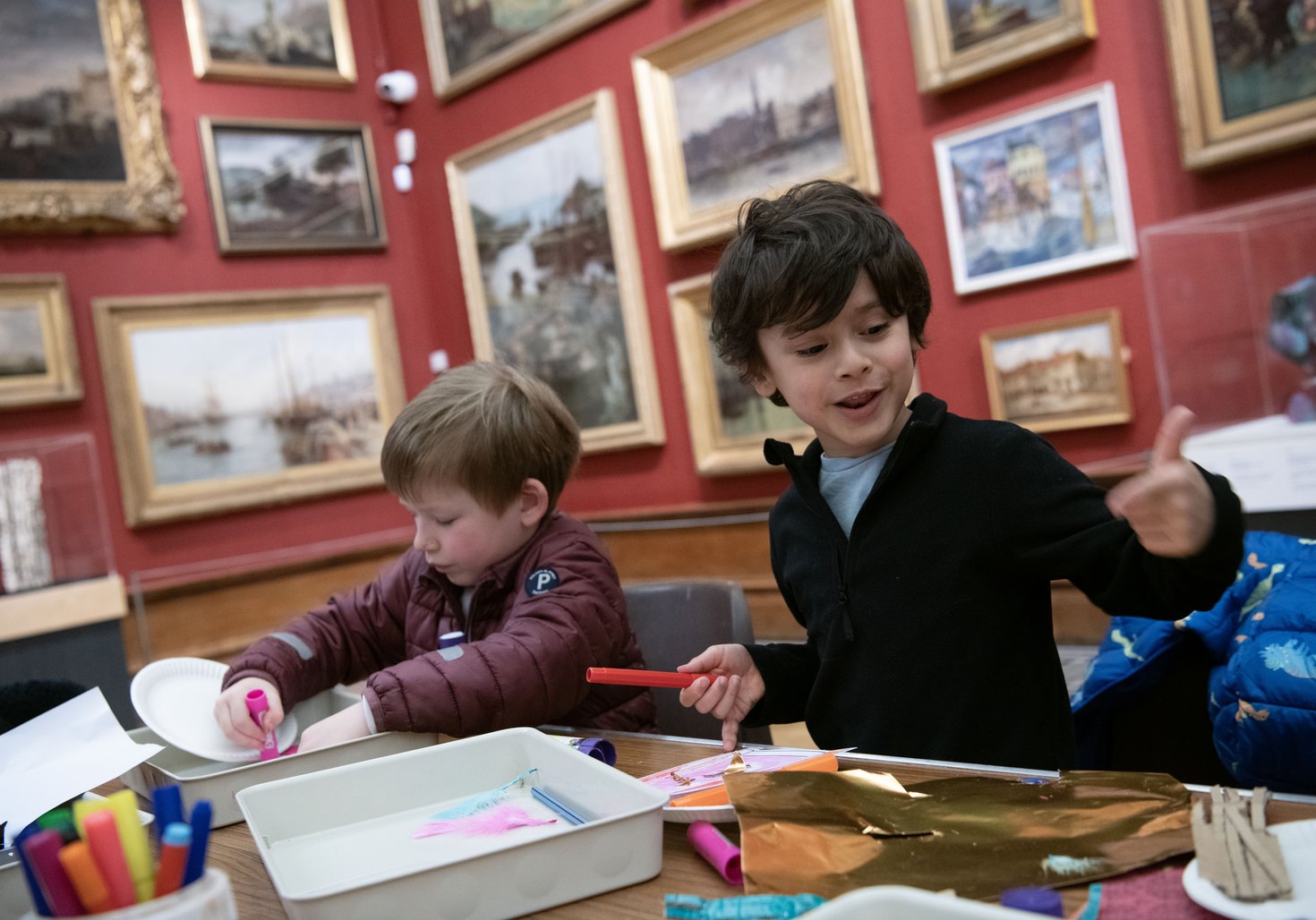 Two children sat at a table playing with craft materials in an art gallery