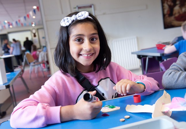 Young girl in pink top and white bow in hair, smiling, doing craft activity