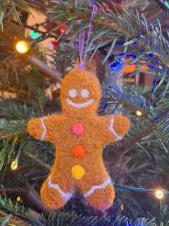A photograph of a needle felted gingerbread man hanging on a Christmas tree.