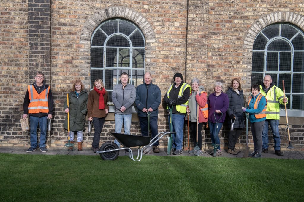 A group of 11 people with gardening tools, some wearing Hi-Vis jackets.
