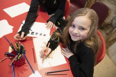 Young girl with long hair sitting at a table drawing with a colouring pencil