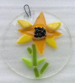 A photograph of a light catcher made of glass. There is a yellow flower design in the middle. 