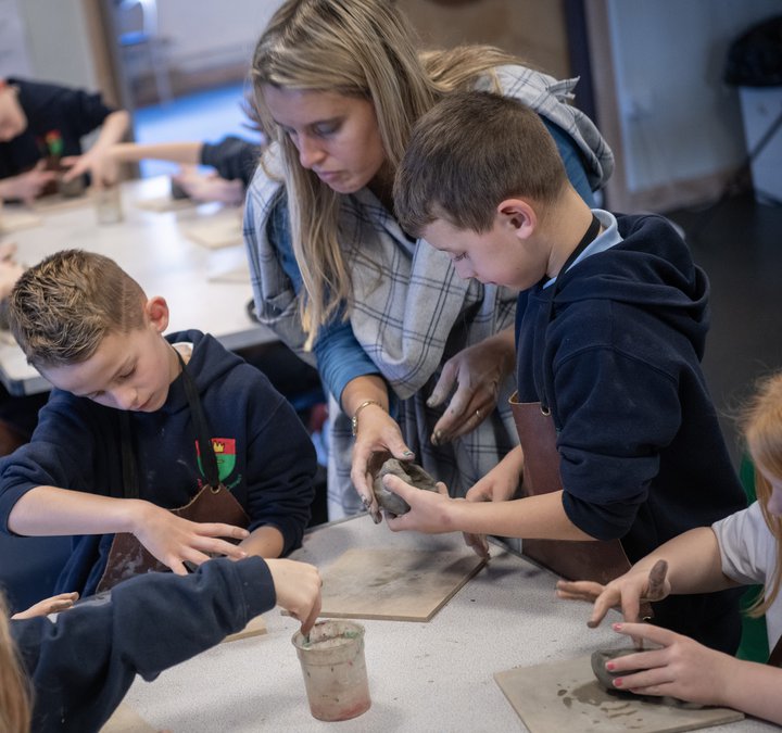 Woman dressed in ancient style clothing helping group of school children to make pottery