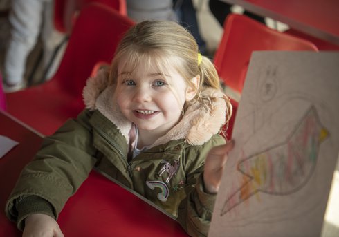 A child holding a drawing looks up at the camera.
