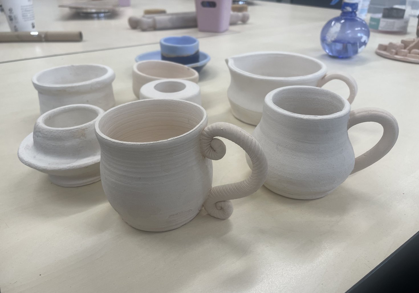 A photograph of a variety of works people are making, such as mugs, cups, and other vessels