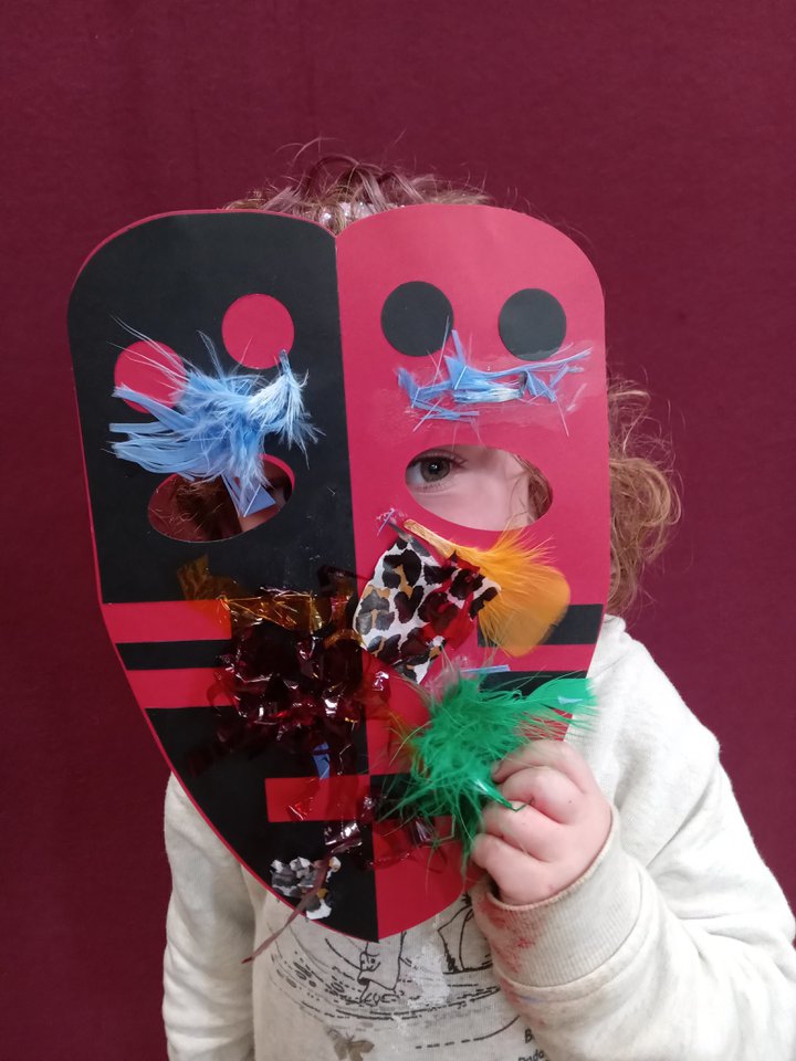 Small child holding an African style mask over their face