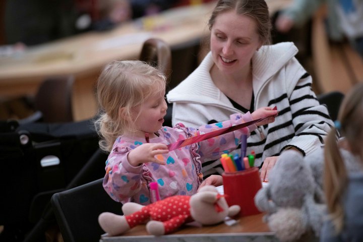 A photograph of a mum and her toddler crafting. The toddler holds a pink metallic ribbon.