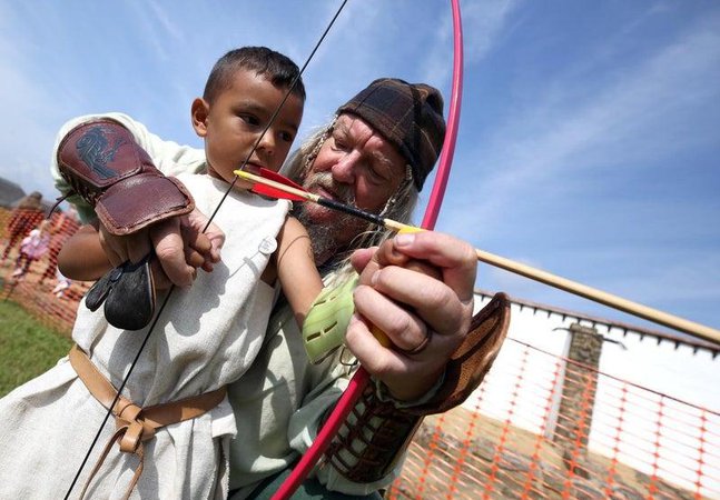 Man helping a young person to learn archery