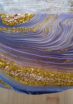 A photograph of an acrylic poured serving board. The decoration has purple swirls and gold decorations, inspired by geodes.