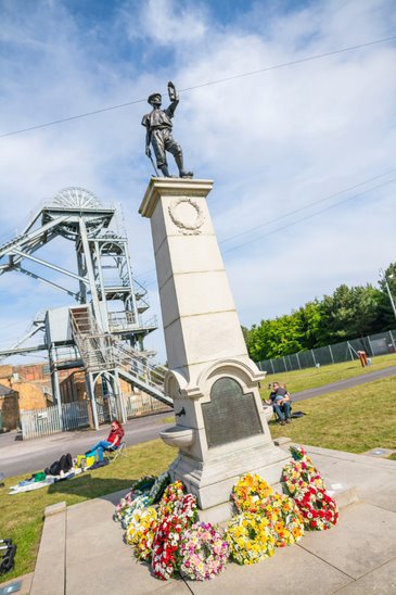 A memorial statue at Woodhorn Museum in front of the colliery buildings adorned with wreaths.
