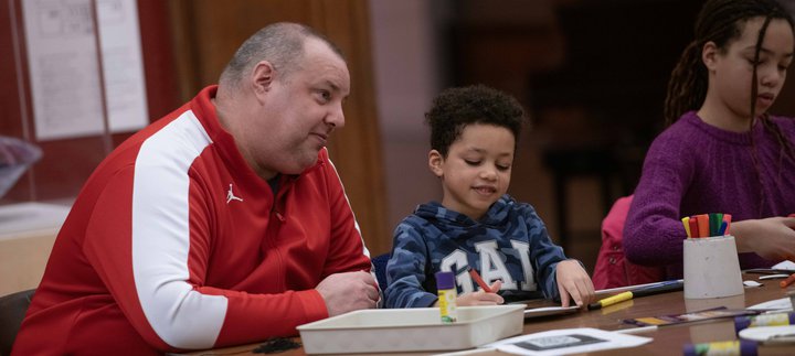 An adult and child sat at a table drawing together.