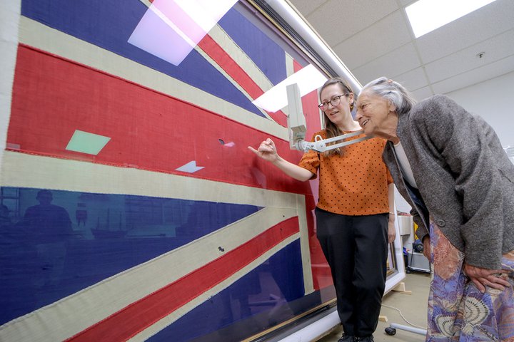 Two women, on older bend and examine a Union flag