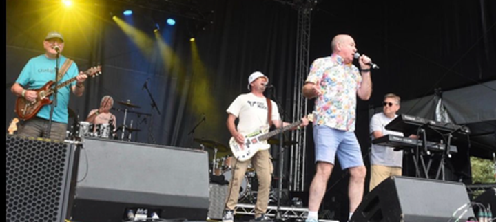 Band performing on stage with instruments and microphones, colorful lights in the background.