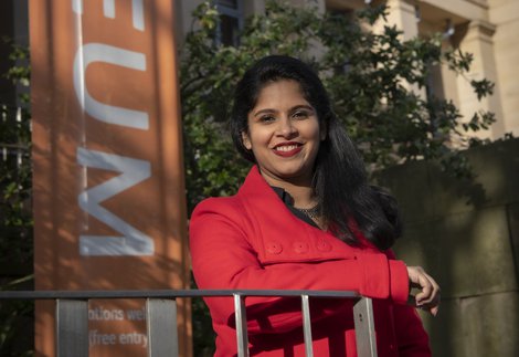 A woman in a red coat stood outside a large sandstone museum building.