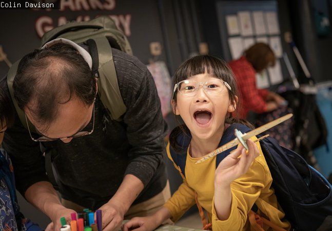 girl in Play Invent gallery holds her creation and laughs at camera 