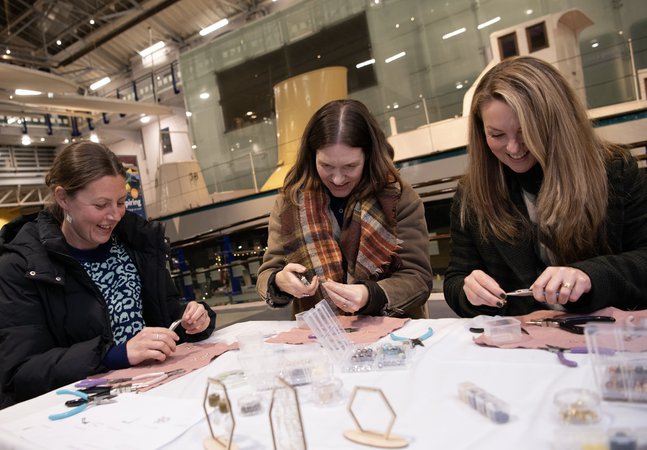 Three women crafting and smiling at Discovery Museum at night