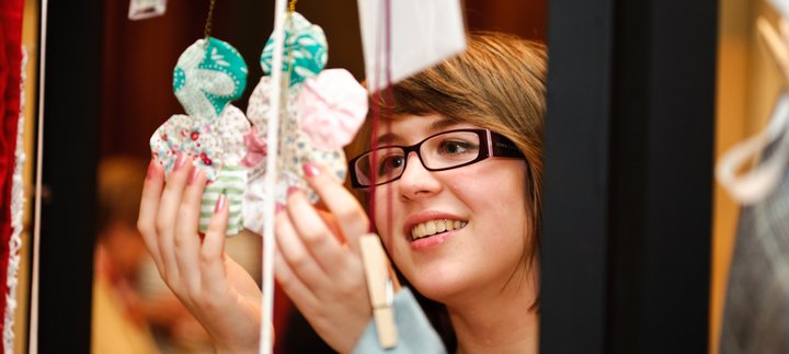 Lady looking at two handmade items hanging from a frame.
