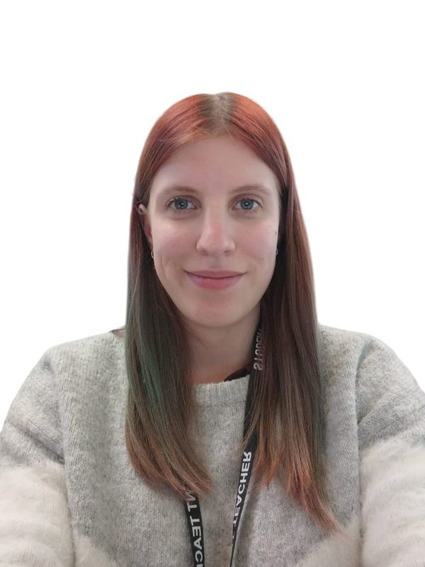A person with long red hair, smiling at the camera. They are wearing a grey and white striped jumper. A person with long red hair, smiling at the camera. They are wearing a grey and white striped jumper.