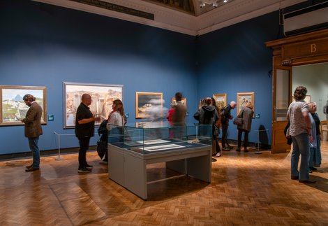 A gallery filled with people looking at paintings on the wall 