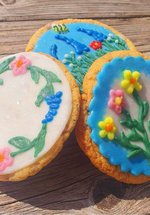 A photograph of three cookies decorated with floral designs. The flowers are pink, yellow, and blue with green stems.