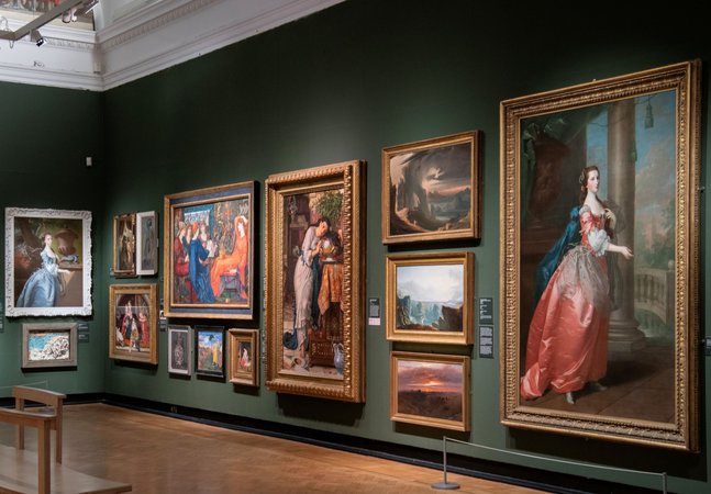 A photograph of the inside of the gallery. Oil paintings in frames hang on a green wall.