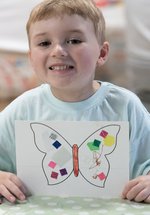 small boy smiles and hold up picture of butterfly