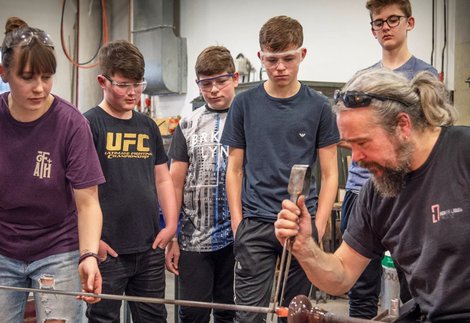 A group of four young people wearing safety make glassglasses watch on as 2 adults use
