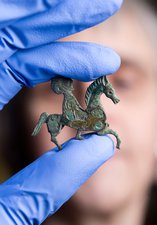 A person is holding a small horse brooch found at Arbeia.