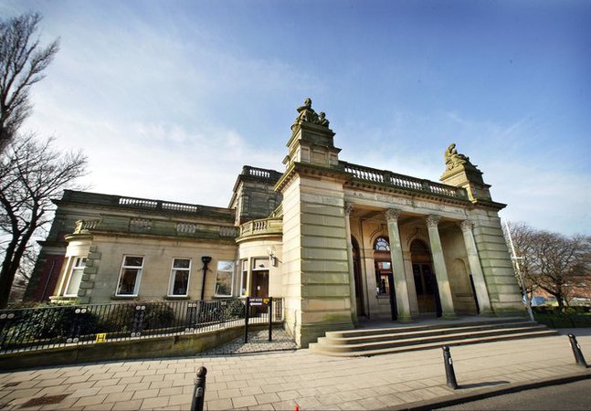 A photograph of the outside of the Shipley Art Gallery. The building is made of a yellow stone with columns in the front.