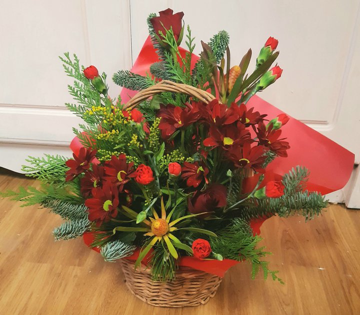 A photograph of a Christmas themed floral arrangement in a wicker basket.