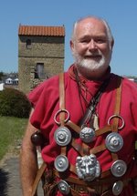 Man in a red tunic, standing with the West Gate in the background