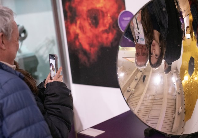 An adult and young person are taking a photo in a concave mirror