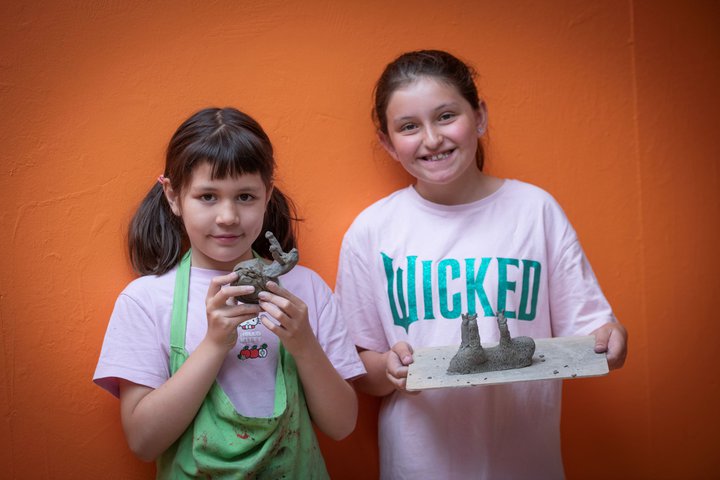Two girls holding up their clay art projects.