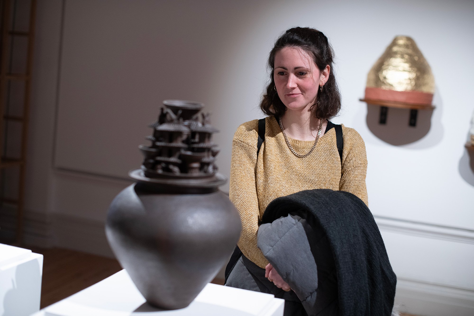 Woman in gold jumper looks at a grey vase