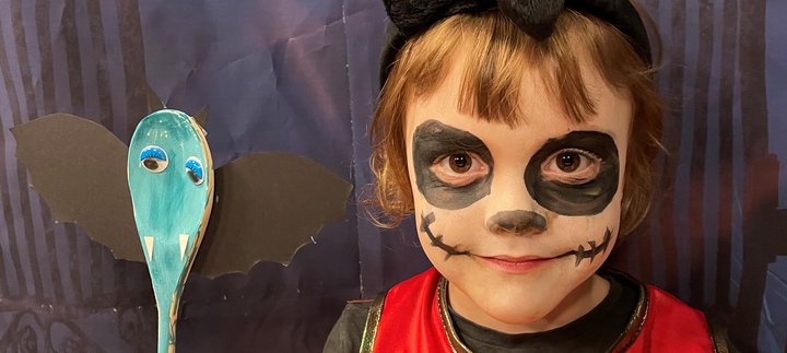 Small girl with spooky face paint holds a bat spoon