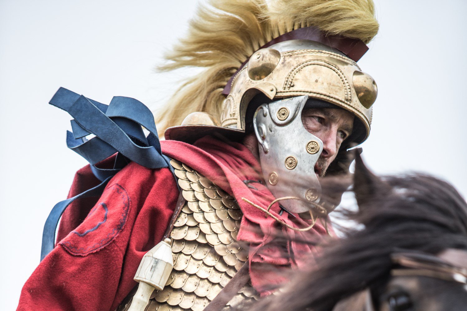 A man dressed in the uniform of a Roman soldier with a helmet, riding a horse.