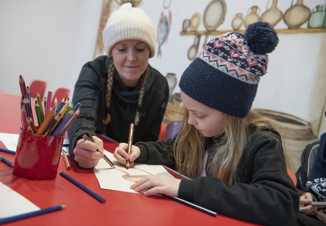 Woman and young girl wearing woolly hats sitting at a table doing a craft activity