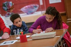 A photograph of a girl with long braids and a young boy with short hair doing crafts. 