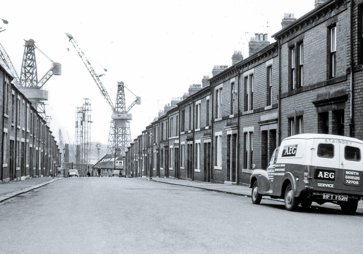 Black and white photo of street with terraced housing leading to shipbuilding yard and cranes