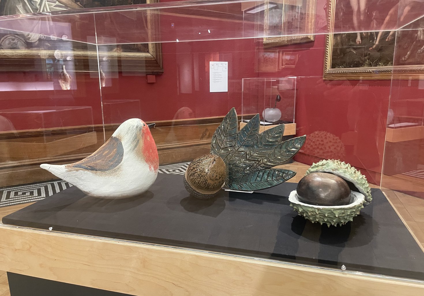 A photograph of three ceramic works in a display case, showing a robin, an acorn, and a conker