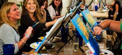 a group of people painting their own canvases with wine glasses in hand