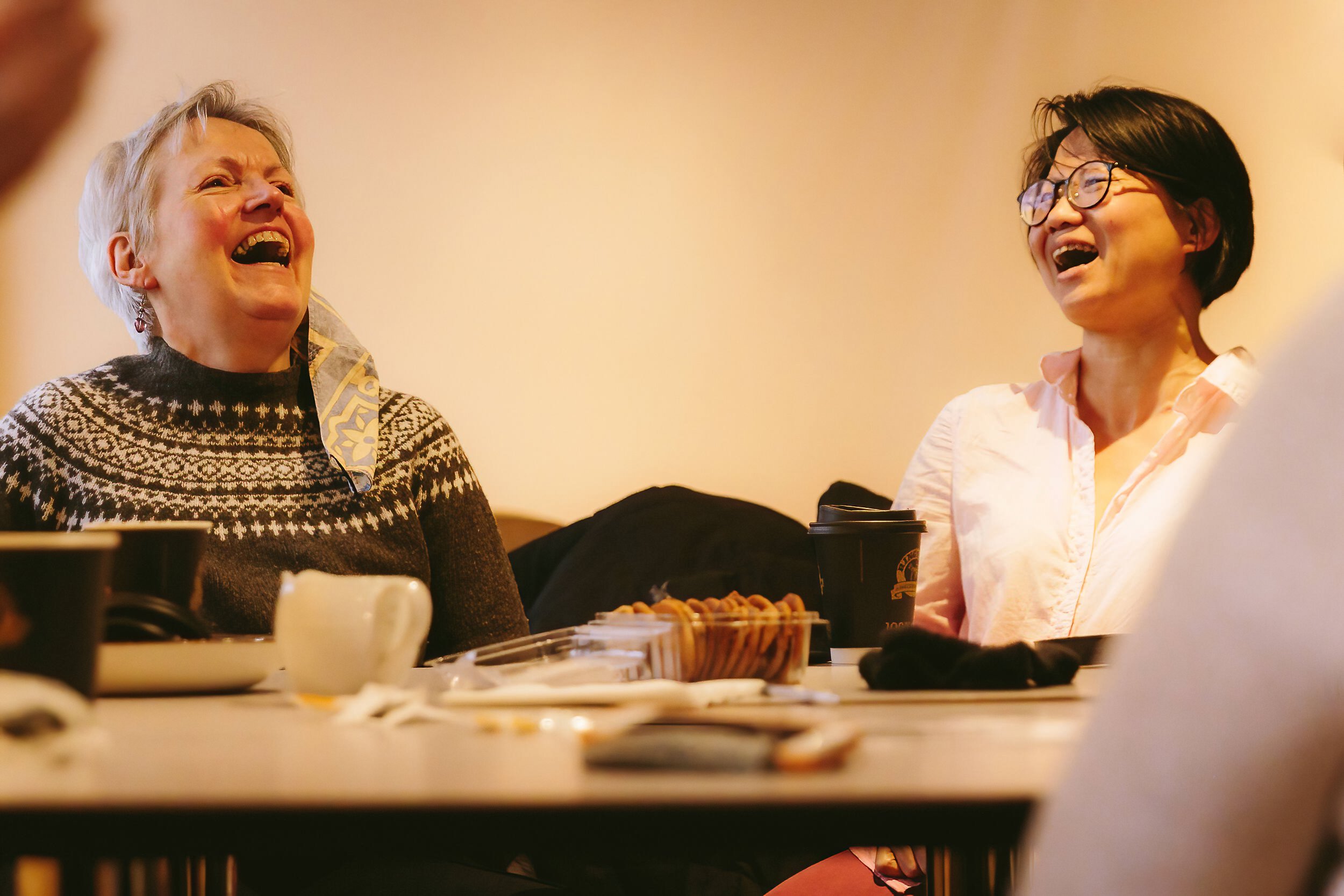 Two women sat at a table laughing to each other.