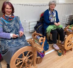 Two women sitting on chairs with spinning wheels