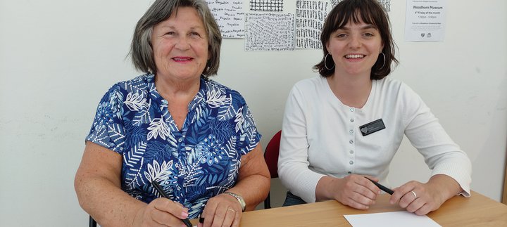 Two Chat Time Volunteers sitting at a desk and smiling at Woodhorn Museum