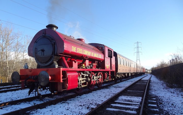 Red steam locomotive pulling passenger carriages on snow covered railway